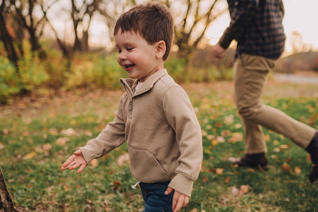 a little boy in a beige sweatshirt runs through a field in Blackwell Forest Preserve
