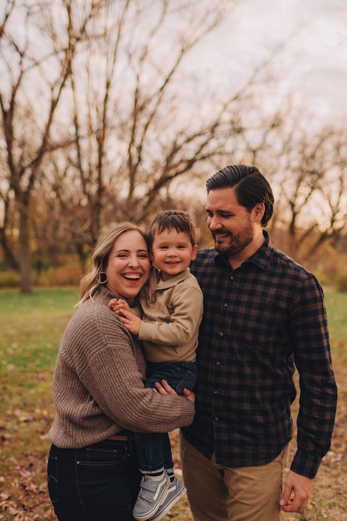 A family laughs and smiles together while looking at the camera, they hold close to one another at a forest preserve in Wheaton