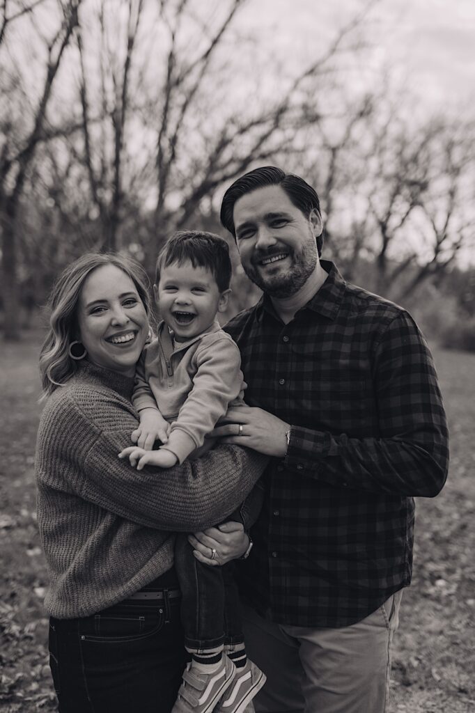 A family laughs and smiles together while looking at the camera, they hold close to one another at a forest preserve in Wheaton