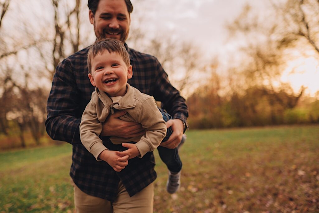 A man holds his little boy up like superman and runs with him through the forest preserve in Wheaton illinois
