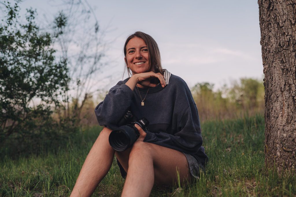 A photo of Marisa, photographer of Msav Photo, sitting in the grass and smiling.